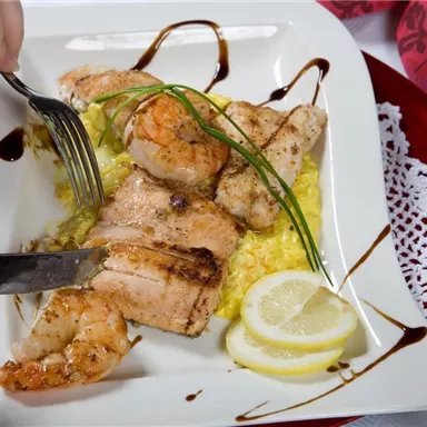 An appetizing dish with grilled fish and shrimp on a bed of yellow rice. Fresh lemon slices and herbs garnish the plate.