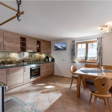 Eine moderne Küche mit Holzschränken und einem großen Fenster, das Tageslicht hereinlässt. Ein Essbereich mit einem runden Tisch und Stühlen vervollständigt den Raum.