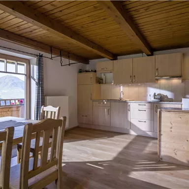 Eine helle und moderne Küche mit Holzdecke und offenen Regal. Der angrenzende Essbereich bietet einen schönen Blick auf die Berge.