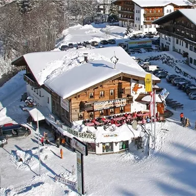 A cozy wooden house in a snowy environment. The building is surrounded by snow and there are many skiers nearby.