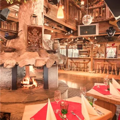 A cozy restaurant with an open fireplace and rustic wooden furniture. The tables are lovingly set, creating an inviting atmosphere.
