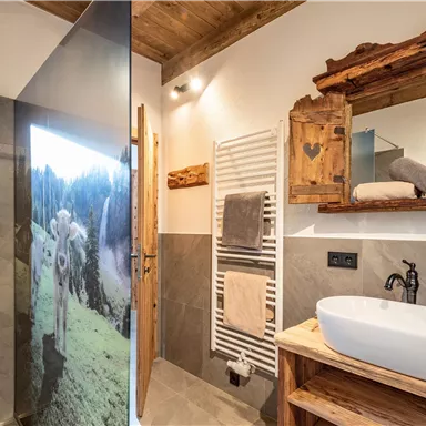 Ein gemütliches Badezimmer im Almchalet mit einer Dusche und einem Holzwaschtisch. Eine helle Atmosphäre durch natürliche Materialien und eine stilvolle Gestaltung.