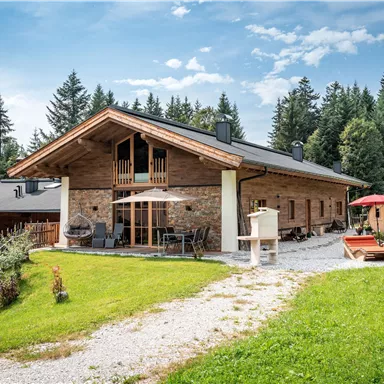 Das Chalet Riederhäusl inmitten von grünen Wiesen und hohen Tannen. Die Umgebung ist ruhig und einladend, ideal für einen erholsamen Aufenthalt.