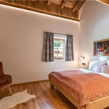 Schlafzimmer mit einem Doppelbett und Holzdekor. Die Wände sind hell und es gibt einen Fernseher sowie einen gemütlichen Sessel.