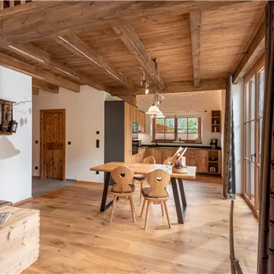 Die Küche des Almchalet Hausruck mit Holzmöbeln und großen Fenstern, die viel Licht hereinlassen. Der Boden ist aus Holz, und es gibt einen einladenden Esstisch mit Stühlen.