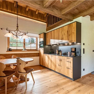 Die Küche des Almchalet Riederhäusl mit Holzschränken und einer gemütlichen Essecke. Das helle, einladende Design schafft eine warme Atmosphäre.