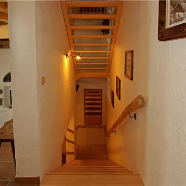 Eine helle Treppe führt in einen offenen Raum. An den Wänden hängen Bilder und das Licht sorgt für eine angenehme Atmosphäre.