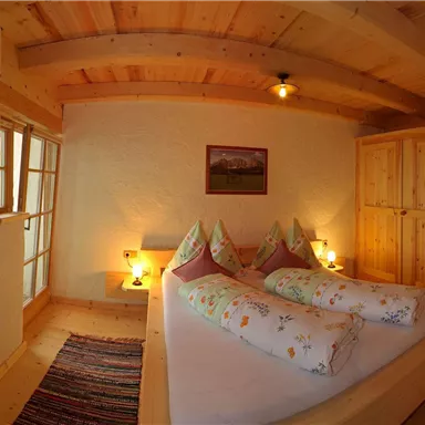 Ein gemütliches Schlafzimmer mit Holzdecken und warmem Licht. Das Zimmer ist mit zwei Betten und einem großen Kleiderschrank ausgestattet.