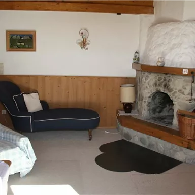 A cozy living space with a stone oven and a blue couch. There are pictures hanging on the wall, and there is a wooden table with chairs.