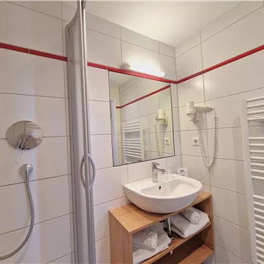 A modern bathroom with a shower and sink. The walls are tiled and there is a towel warmer.