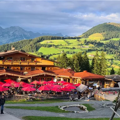 A cozy restaurant in the mountains with red umbrellas. The surroundings are green and hilly, ideal for a view of nature.