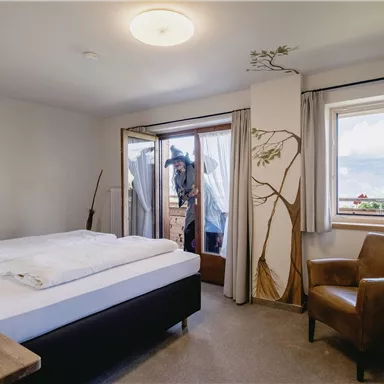 A modern bedroom with a double bed and a cozy armchair. Large windows provide a view of the surroundings, and there is a stylish wall decoration.