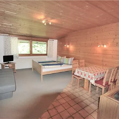 Ein gemütlicher Raum mit Holzwänden, einem Doppelbett und einem Esstisch. Es gibt ein Sofa, einen Fernseher und eine kleine Küchenzeile.