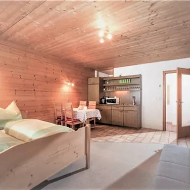 Ein gemütliches Zimmer mit Holzwänden und zwei Betten. Es gibt eine kleine Küchenzeile und einen Esstisch mit Stühlen.
