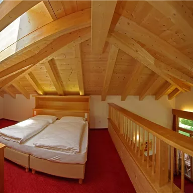 A bright and cozy bedroom with wooden beams and a large window. The room has a double bed and an open, inviting layout.