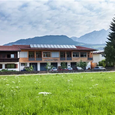 A modern building surrounded by meadows and trees in a mountainous landscape. The clouds in the sky give the scene a calm atmosphere.