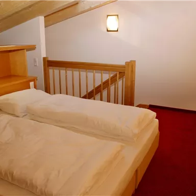 A bright bedroom with two single beds and wooden details. The walls are simple and the atmosphere is cozy.