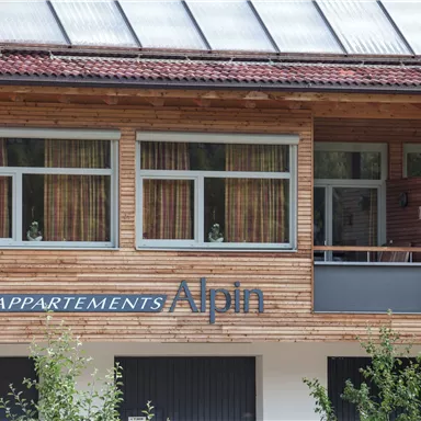 A modern wooden facade with large windows. The inscription "APPARTEMENTS Alpin" is clearly visible.