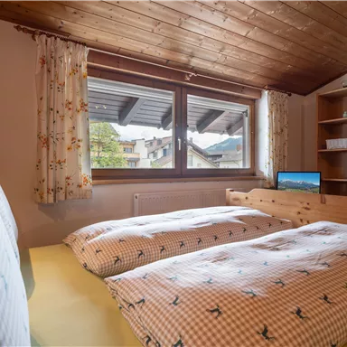 Ein gemütliches Schlafzimmer mit zwei Betten und einem Fenster, das nach draußen blickt. Die Holzwände und der rustikale Stil schaffen eine einladende Atmosphäre.