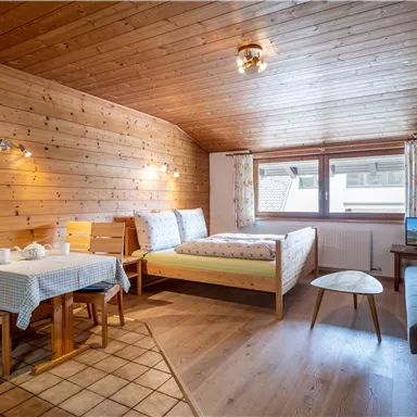 Ein gemütliches Zimmer mit Holzwänden, einem Doppelbett und einem kleinen Esstisch. Ein Fernseher und ein Sofa sorgen für zusätzlichen Komfort.
