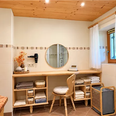 Ein modernes Badezimmer mit Holzdecke und großer Spiegelleuchte. Der Raum ist stilvoll eingerichtet mit einem Holzschreibtisch, Handtüchern und dekorativen Elementen.