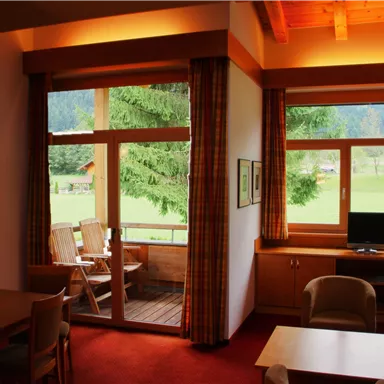 A cozy room with a wooden ceiling and large windows. Outside, a green landscape is visible.