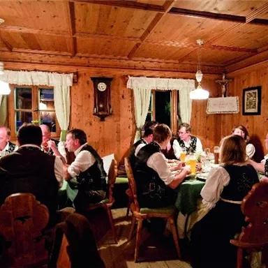A cozy room with a long table where people in traditional costumes eat and celebrate together. Warm light and wooden-paneled walls create an inviting atmosphere.