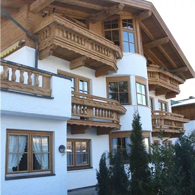 Ein schönes Holzhaus im traditionellen Stil mit Balkonen und großen Fenstern. Umgeben von grünen Sträuchern und einem klaren Himmel.