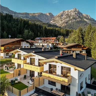Moderne Chalets in einer malerischen Berglandschaft. Die Umgebung ist von Bäumen und majestätischen Bergen umgeben.