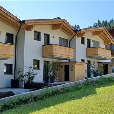Moderne Häuser mit Holzverkleidung in einer grünen Umgebung. Die Architektur ist schlicht und harmonisch in die Landschaft integriert.