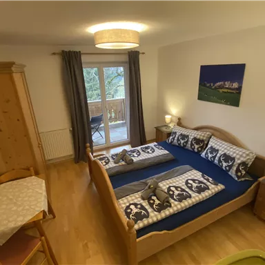 Ein gemütliches Schlafzimmer mit zwei Betten und Holzmöbeln. Der Raum hat einen Balkon und ist hell und freundlich eingerichtet.