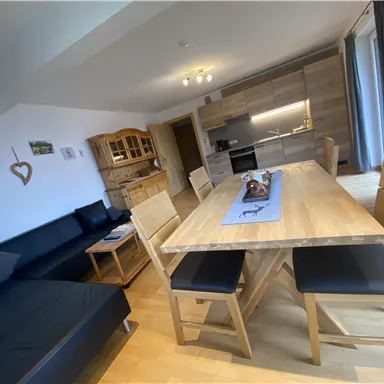 Ein modernes Wohnzimmer mit einer hellen Küche. Es gibt einen großen Holztisch mit Stühlen und einer komfortablen Couch.