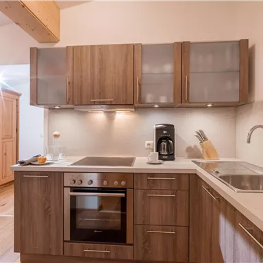 A modern kitchen with wooden cabinets and bright surfaces. Equipped with a stove, a sink, and a coffee machine.