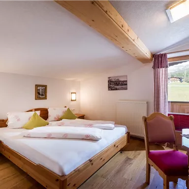 A cozy bedroom with two beds and wooden furniture. A window offers a view of the surrounding nature.