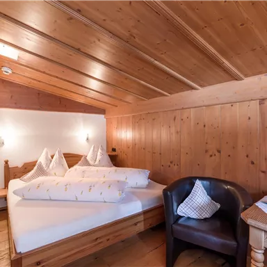 A cozy bedroom with wooden paneling and two beds. There is an armchair and a small table that create an inviting atmosphere.