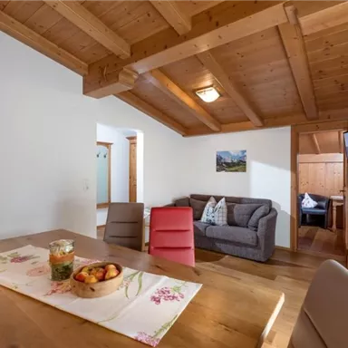 A bright and cozy living kitchen with a wooden ceiling and a large dining table. In the background, you can see a seating area and a television.