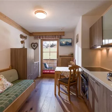 A cozy little kitchen with a dining area and a sofa bed. Large windows provide a view of the outdoors and let in plenty of light.