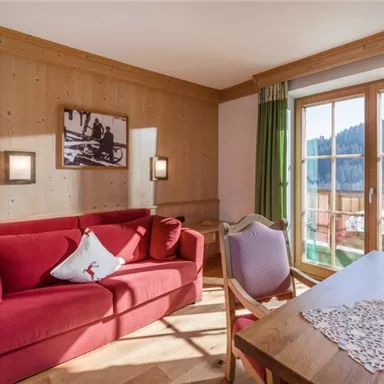 A cozy living room with a red sofa and wooden paneling. The windows offer a beautiful view of the surrounding landscape.