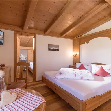 A cozy bedroom with wooden furniture and a large bed. The walls are bright and there is a window that lets in natural light.