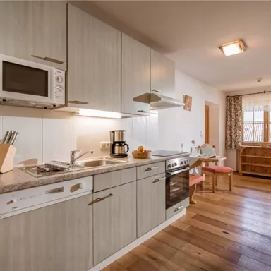 A modern kitchen with light cabinets and wooden flooring. There is a stove, a microwave, and a small dining area.