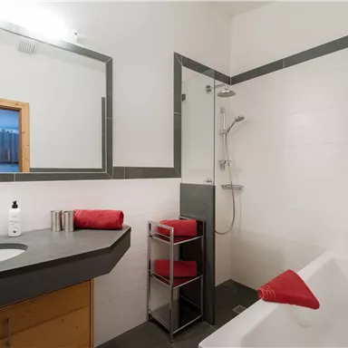 A modern bathroom with a shower, bathtub, and a large mirror. Red towels and toiletries create an inviting atmosphere.