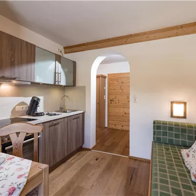 A modern kitchen unit with wooden shelves and a dining table. The room has a cozy seating area and warm wooden decor.