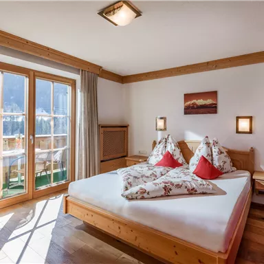 A cozy bedroom with a big bed and colorful pillows. There are windows with a view and warm wooden paneling.