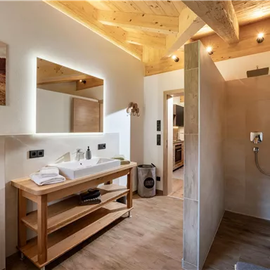 A modern bathroom with a wooden ceiling and a spacious mirror. The shower is bright and elegantly designed, with a minimalist setup.