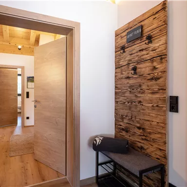An inviting entrance area with wooden panels and a bench. The walls are light, and the door leads to additional rooms.