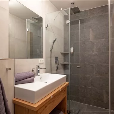 A modern bathroom with a walk-in shower and a sink. The walls are painted in neutral colors and the floor is tiled with gray tiles.