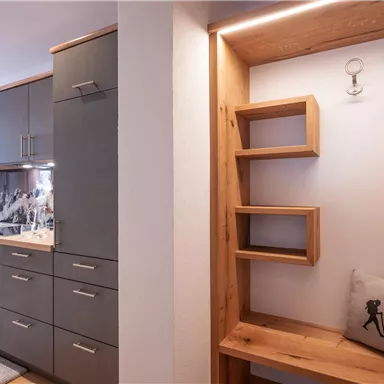 A modern kitchen with gray cabinets and a wooden shelf. The room appears bright and inviting.