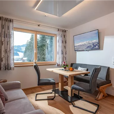 A cozy living space with a seating area and a dining table. Large windows provide a view of the mountains and ensure plenty of daylight.