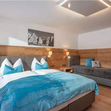 A modern hotel room with a large double bed and a single bed. The walls are made of wood, and the decor is in calming shades of blue and gray.