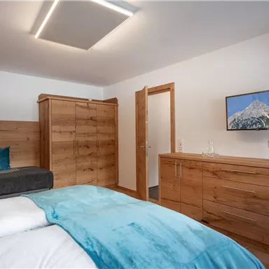 A modern bedroom with wooden furniture and a large bed. A television hangs on the wall and there is a cozy seating area.